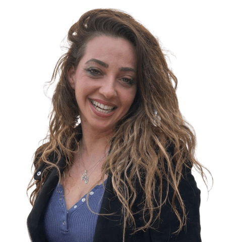 אישה חייכנית עם שיער מתולתל וחום, ז'קט שחור ושרשרת כסף.